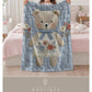 Embroidered-look teddy bear girl baby blanket with floral details on a soft blue quilted background.