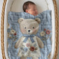 Embroidered-look teddy bear girl baby blanket with floral details on a soft blue quilted background.