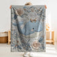 This embroidered look baby blanket features a gentle whale with a delicate bow, surrounded by soft floral elements in calming blue, cream, and natural tones.