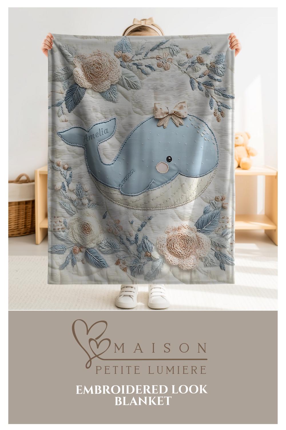 This embroidered look baby blanket features a gentle whale with a delicate bow, surrounded by soft floral elements in calming blue, cream, and natural tones.