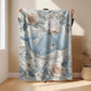 This embroidered look baby blanket features a gentle whale with a delicate bow, surrounded by soft floral elements in calming blue, cream, and natural tones.