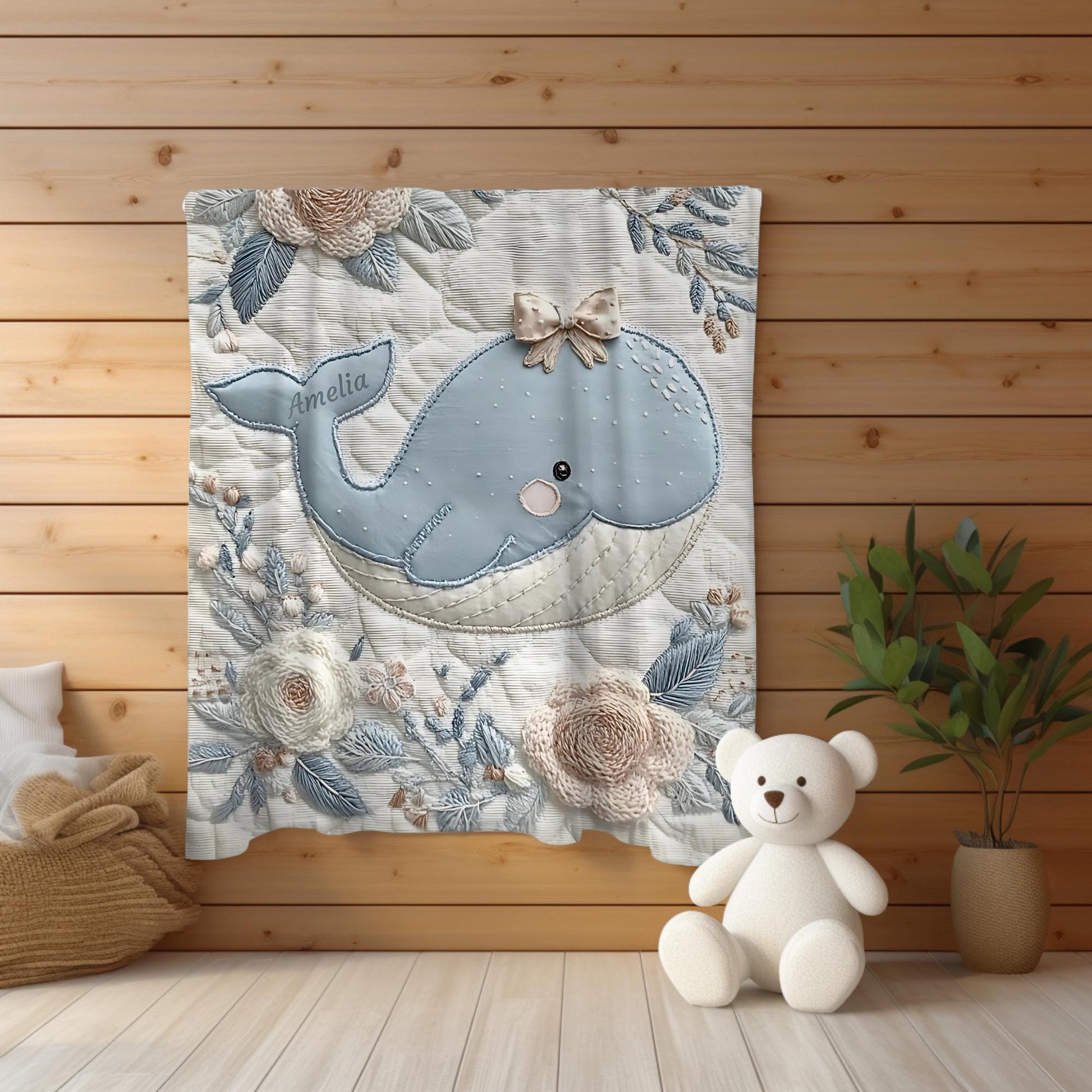 This embroidered look baby blanket features a gentle whale with a delicate bow, surrounded by soft floral elements in calming blue, cream, and natural tones.
