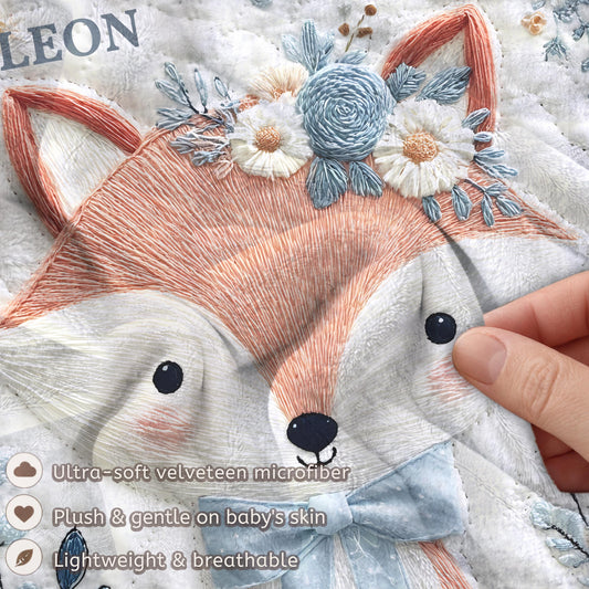 Embroidered-look fox baby blanket with soft floral crown and gentle blue–peach stitched details on a neutral background.