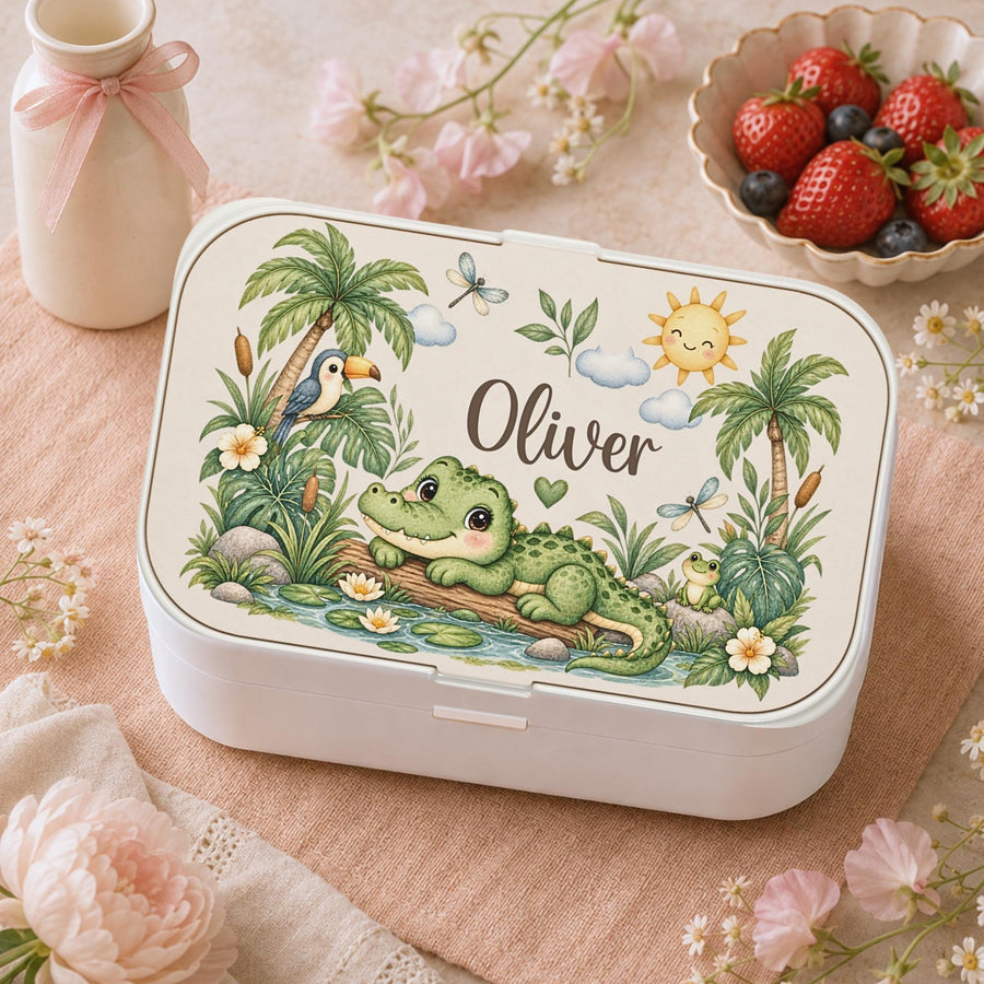 Personalized Crocodile Bento Lunch Box featuring a charming watercolor fine art print with a sweet crocodile, tropical palm trees, a toucan, frog, dragonflies, water lilies and a smiling sun. Customized with your child’s name, this practical kids lunchbox is perfect for daycare, preschool, kindergarten, school, picnics and everyday adventures.