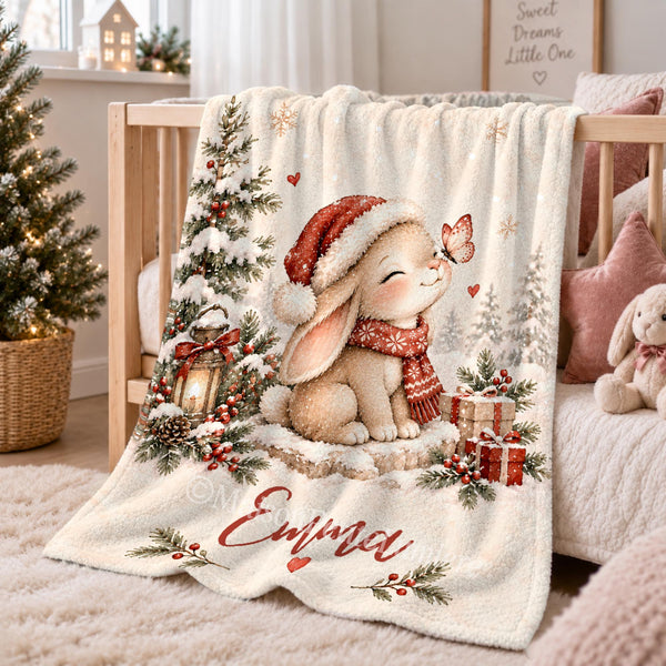 Personalized Christmas bunny baby blanket featuring a watercolor bunny in a Santa hat and knitted scarf, a pink butterfly, snowy pine trees, a glowing lantern and wrapped gifts.