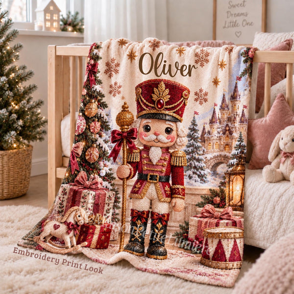 Personalized Christmas Nutcracker Baby Blanket with an embroidered-look print featuring an adorable classic Christmas nutcracker in a rich cranberry red and gold uniform, surrounded by a magical snowy Christmas landscape, fairytale castle, decorated Christmas trees, glowing lantern, presents, rocking horse, snowflakes and festive ornaments.